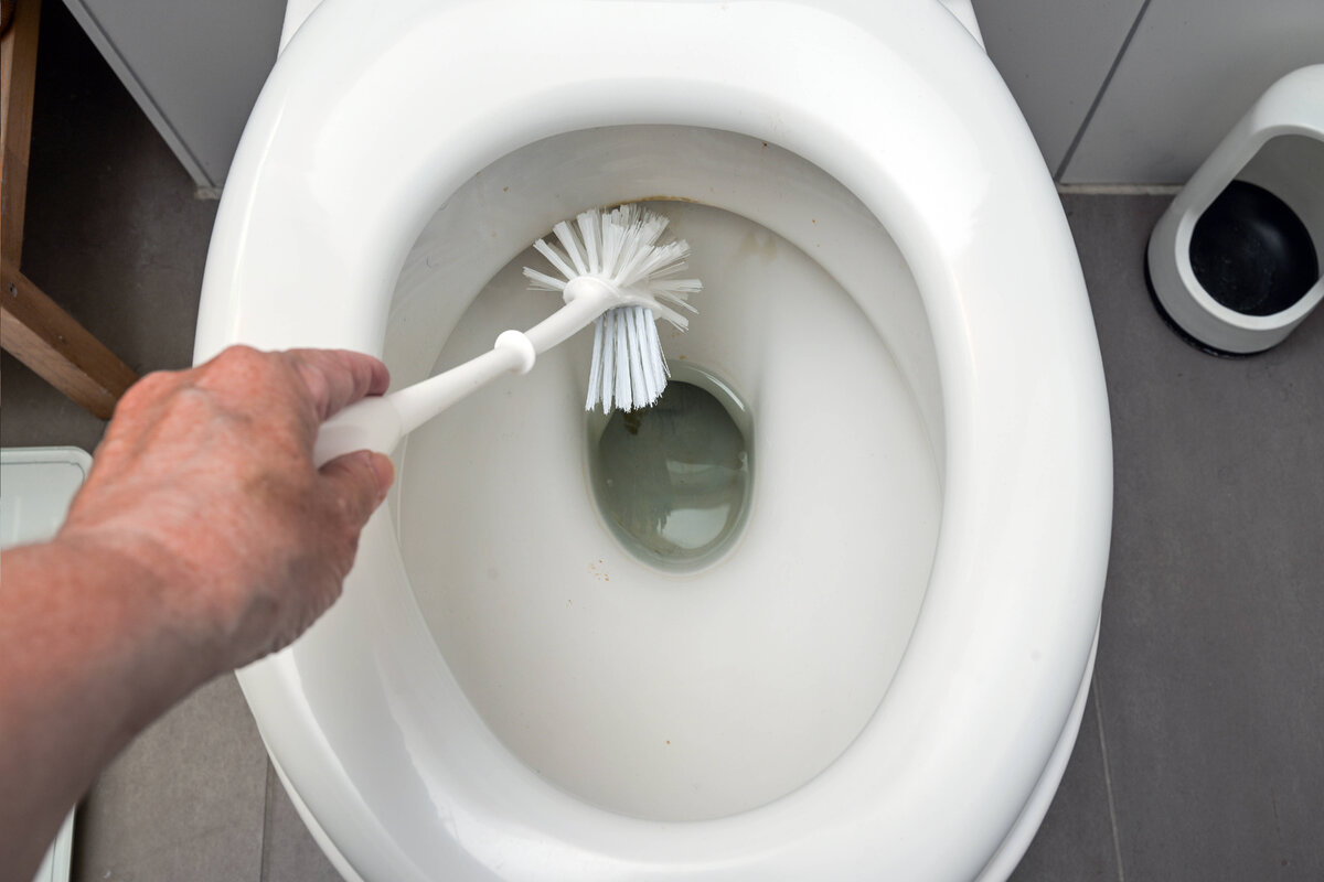 iemand schrobt de kalkaanslag in het toilet weg